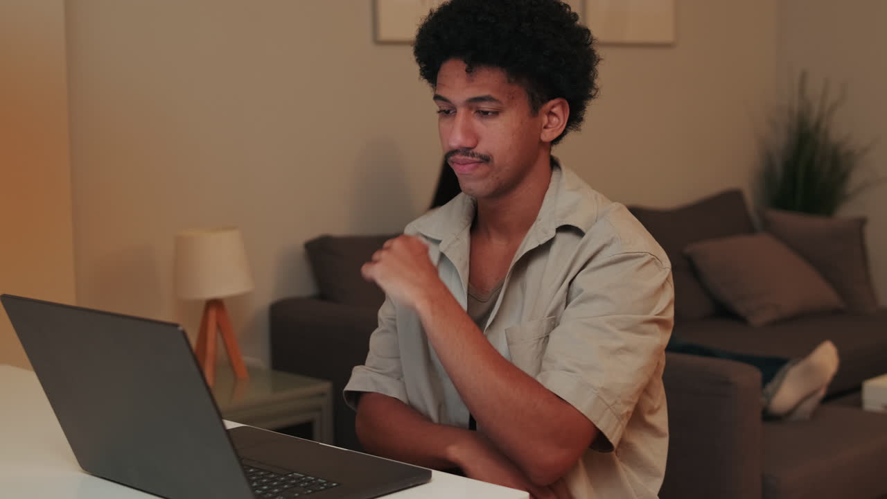 Young Man Typing and Thinking While Working on Laptop at Home