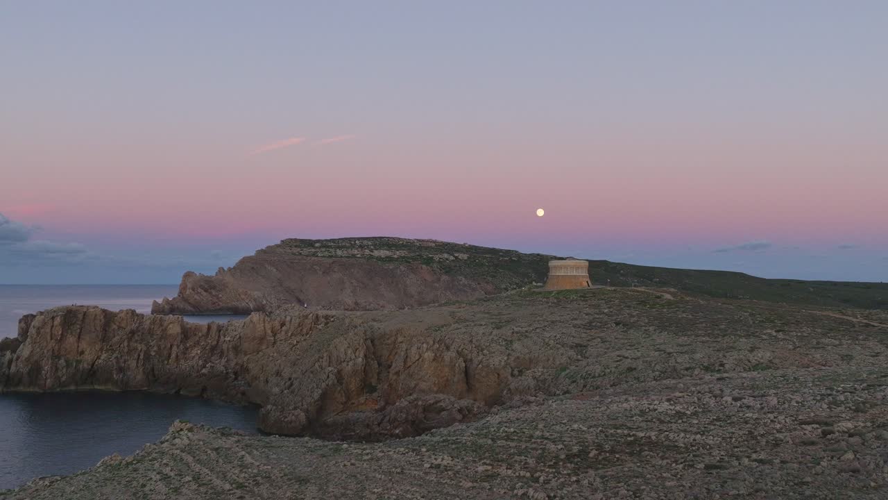 Lyserød solnedgangshimmel over Fornells på Menorca, Spanien, med filmisk flyvning omkring et gammelt forsvarstårn.