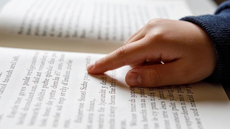 Tracing kid right hand at desk, sliding finger over book text, learning, dark sleeve, copy space