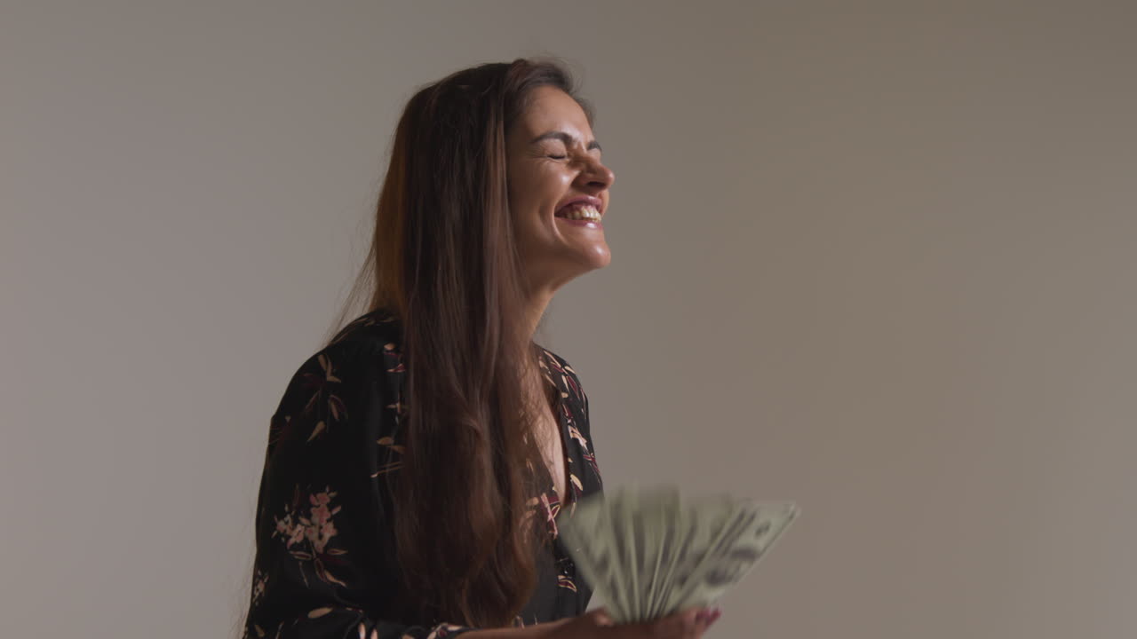 Studio Shot Of Excited Woman Celebrating Winning Cash Prize Throwing Handful Of 100 Dollar Bills In The Air