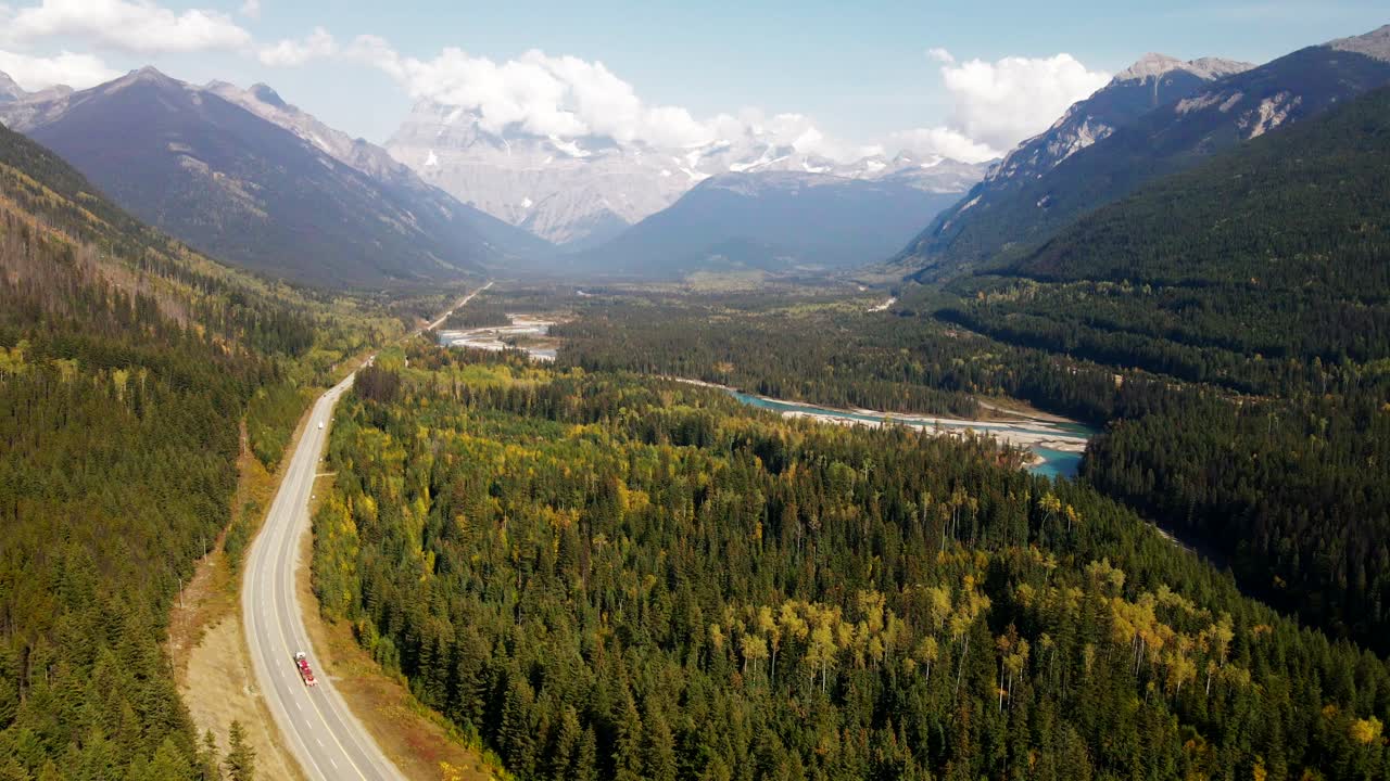 magnificent dolly backwards zoom shot of Mount Robson Provincial Park in the autumn on a mix of sun and cloudy day with mountains in the background and the yellowhead highway with light traffic