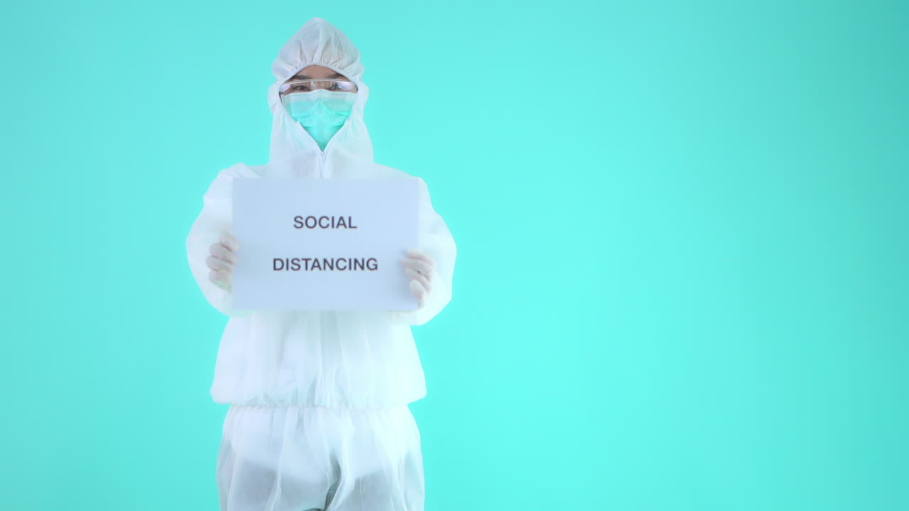 Person in Protective Medical Clothing Showing Social Distancing Motto on White Board, Isolated on Turquoise Background
