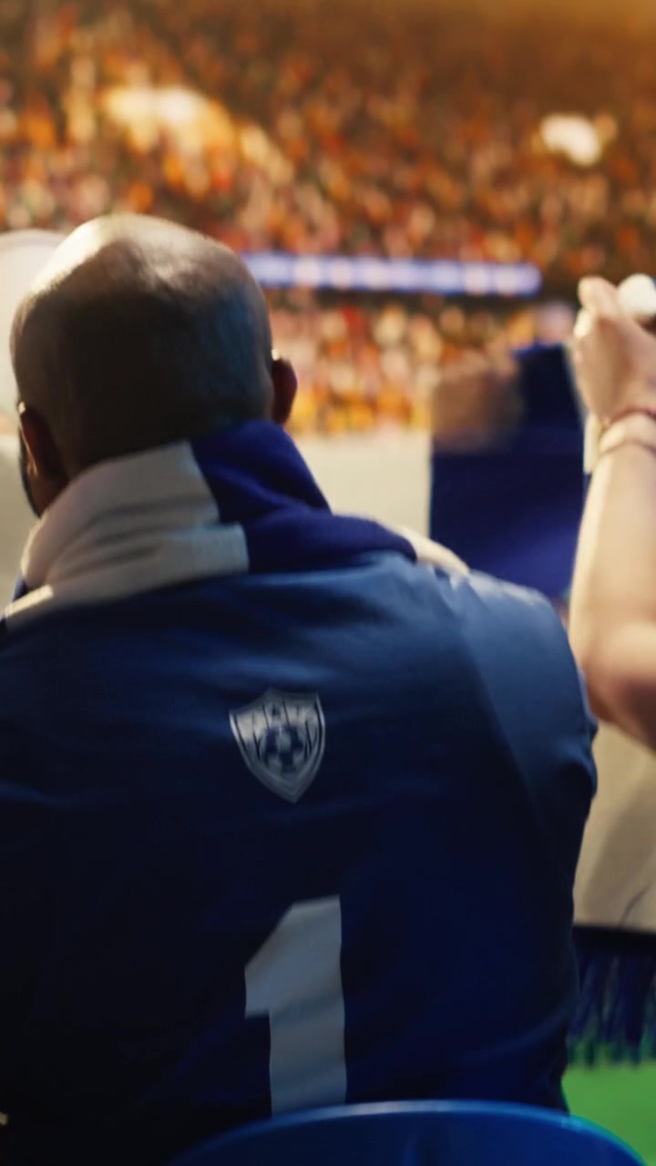 Vídeo vertical. Close-up de torcedores de futebol cantando com vuvuzelas em um estádio lotado.
