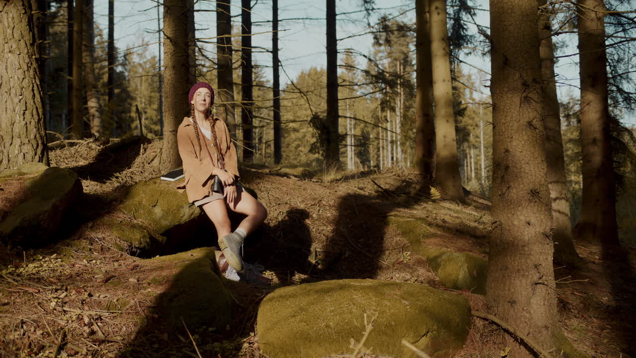 Frau sitzt an einem sonnigen Tag auf einem Felsen im Wald
