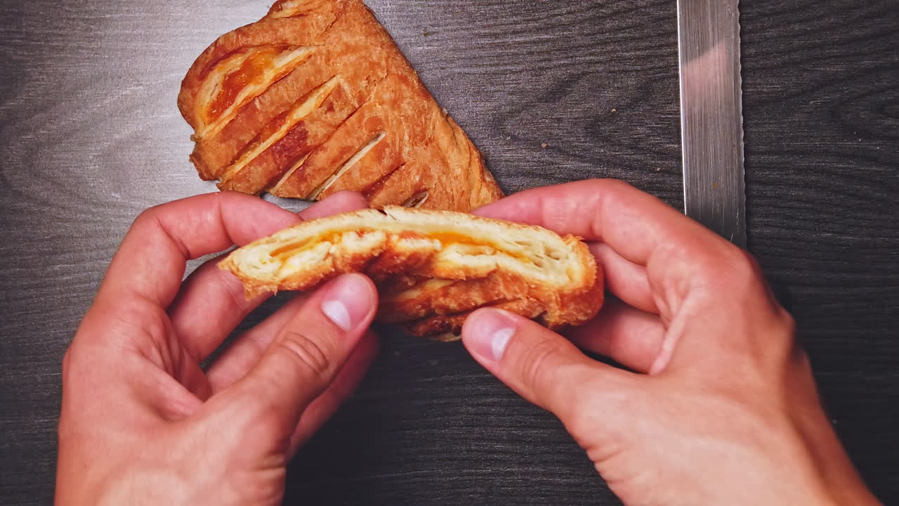 Overhead shot of a young caucasian man eating e piece of a bread from a wooden black table
