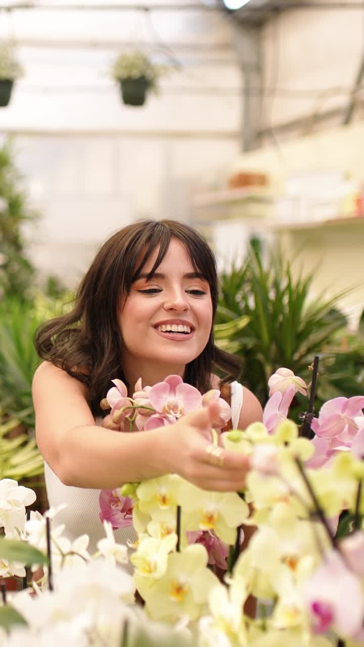 Woman gardener smiling and taking care of orchids in greenhouse. Vertical