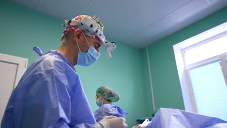 professional surgeon at eyelid operation. doctor in headlight talks to camera gesturing with his hand. low angle view.