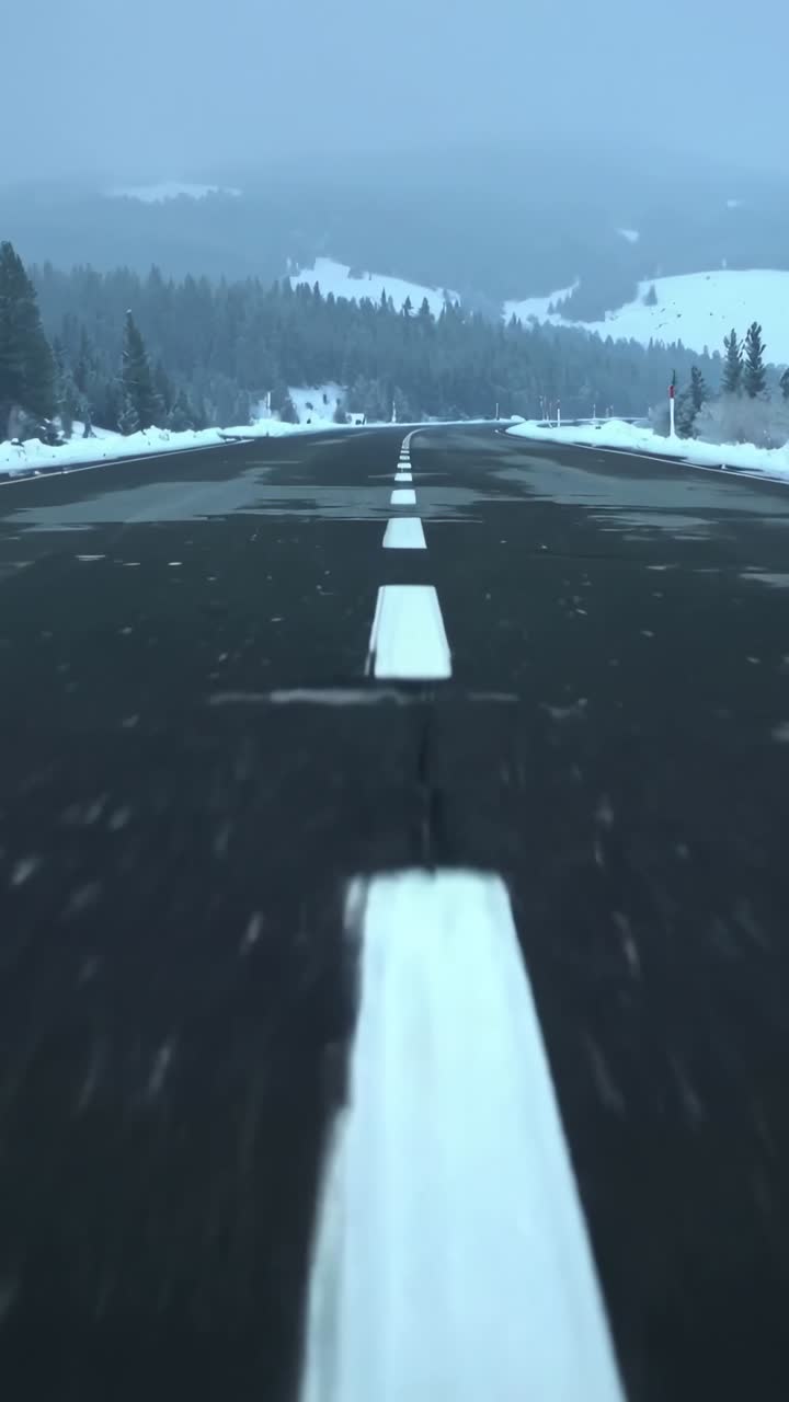 Vertical video: Starting low camera rolling down snow-lined mountain road, recording centerline