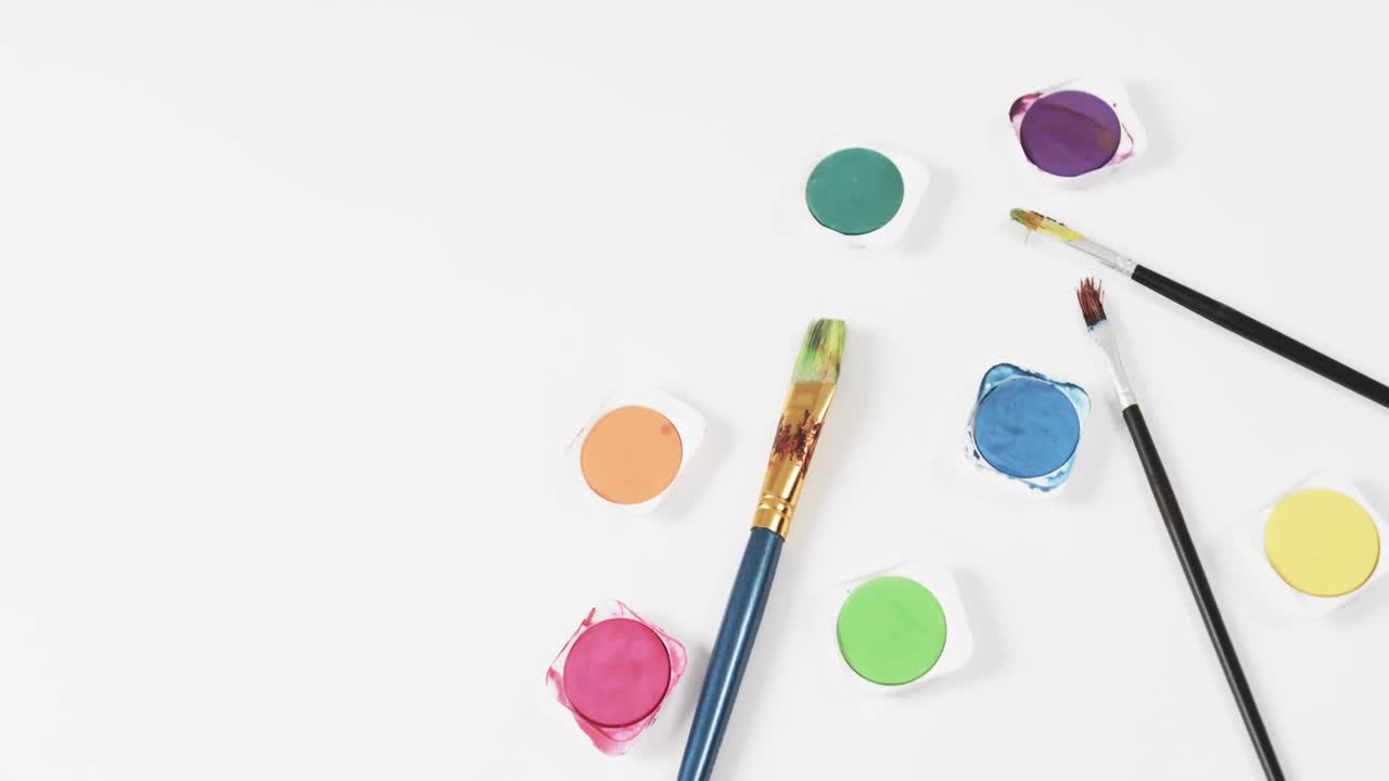 primer plano de pinturas y pinceles sobre fondo blanco con espacio de copia, en cámara lenta