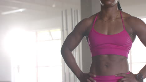 standing in gym, strong fit woman wearing pink sports bra, showing muscular physique, copy space