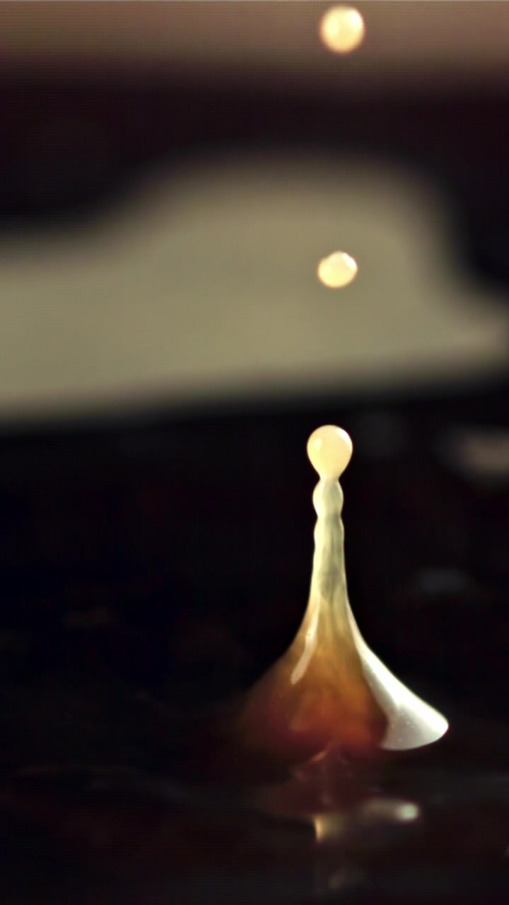 Em câmera lenta, gota de líquido espirrando e formando uma coluna ascendente.