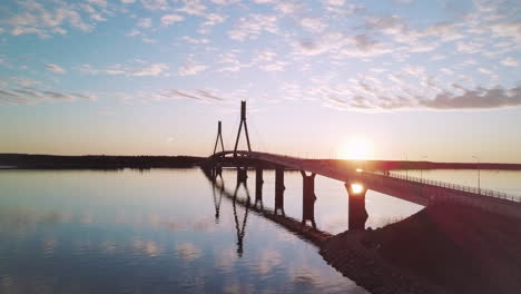 aerial orbiting shot car crossing replot bridge during sunset with mirror reflection on water, finland