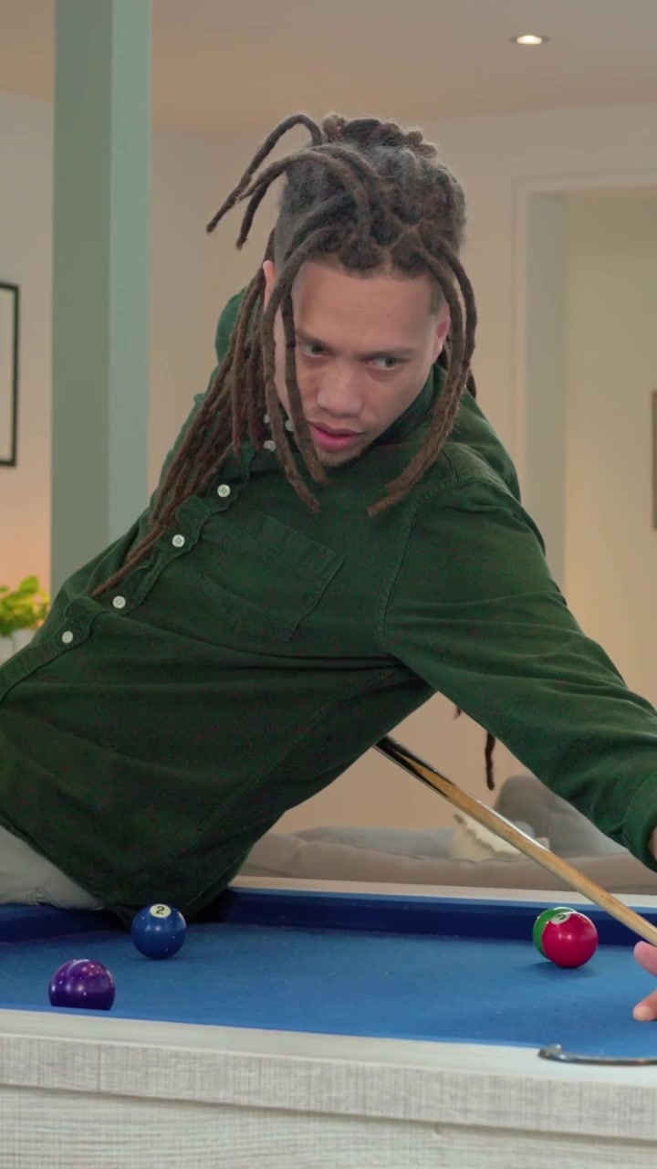 Vertical video: Spinning cue, man in green shirt lining shot to sink ball at blue table in home