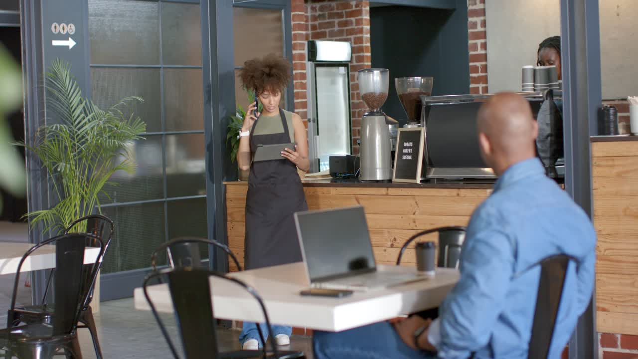 Barista mulher atendendo ao telefone enquanto verifica o tablet e confirma o pedido no balcão.