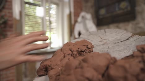 a close-up of potter putting clay onto wooden stump for creating modern art style ceramic sculpture in his studio