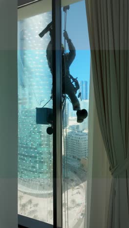 inside a skyscraper apartment while a window cleaner washes the outside while rappelling from a rope - vertical