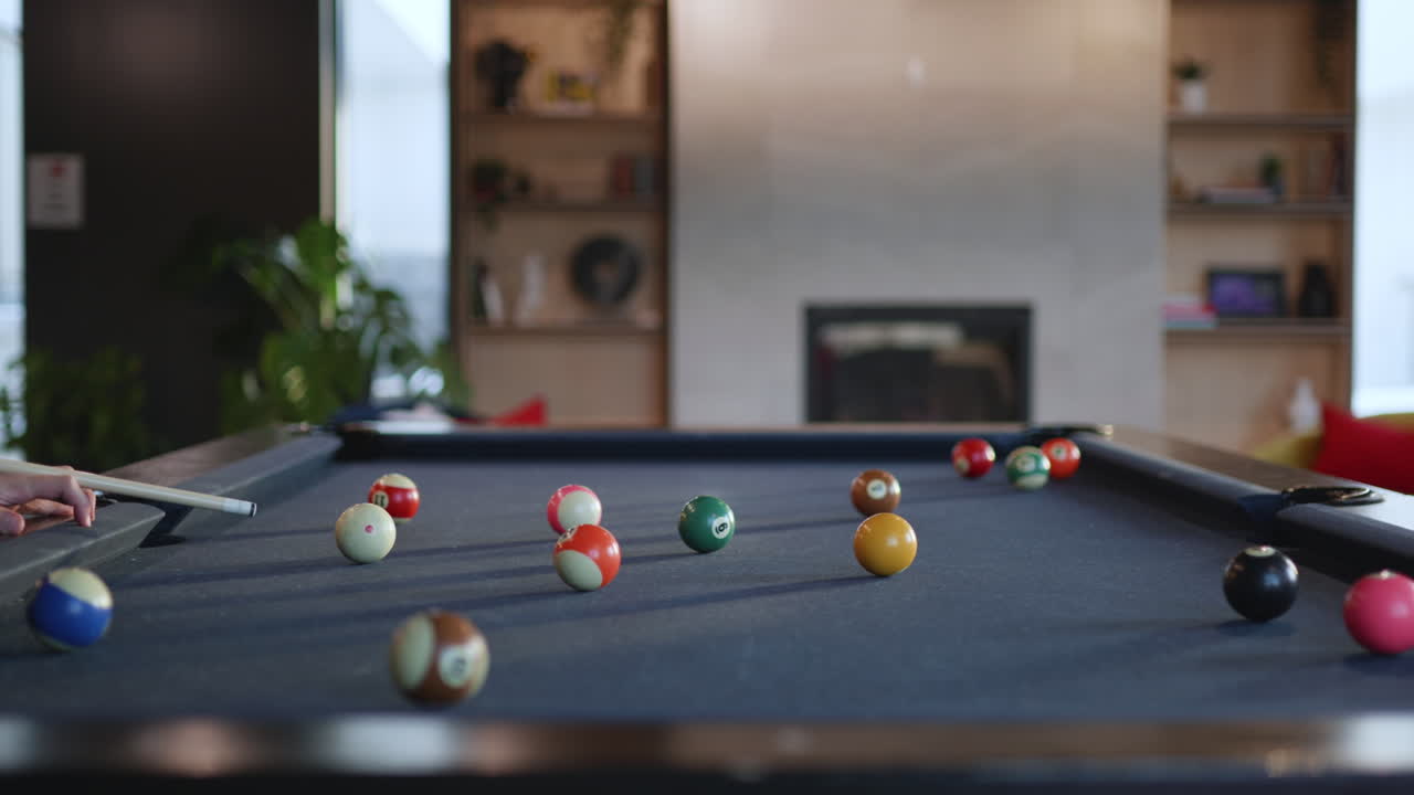 Colorful billiard balls are scattered across a pool table in a modern lounge. A cozy atmosphere surrounds the table as friends enjoy their time during a leisurely afternoon.