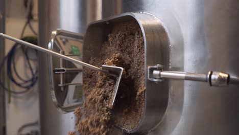 pulling out spent grains of malt from the tank with a stainless scraper in the brewery - close up slowmo