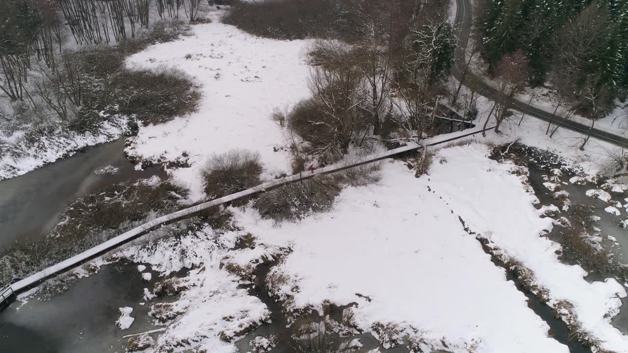 눈으로 뒤덮인 숲과 얼어붙은 호수 옆 나무 길을 달리는 사람의 공중 전망