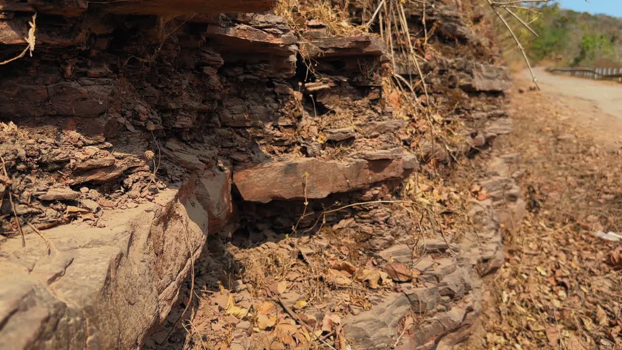 La telecamera si muove lungo strati di roccia sedimentaria esposti su un pendio, rivelando strati orizzontali e formazioni erose modellate da una graduale deposizione di sedimenti.