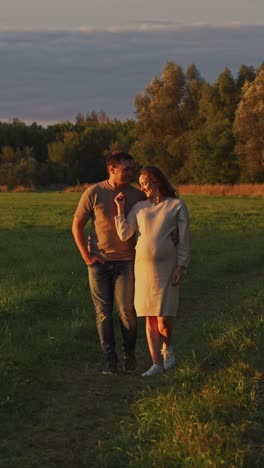 pregnant couple walking in a field at sunset