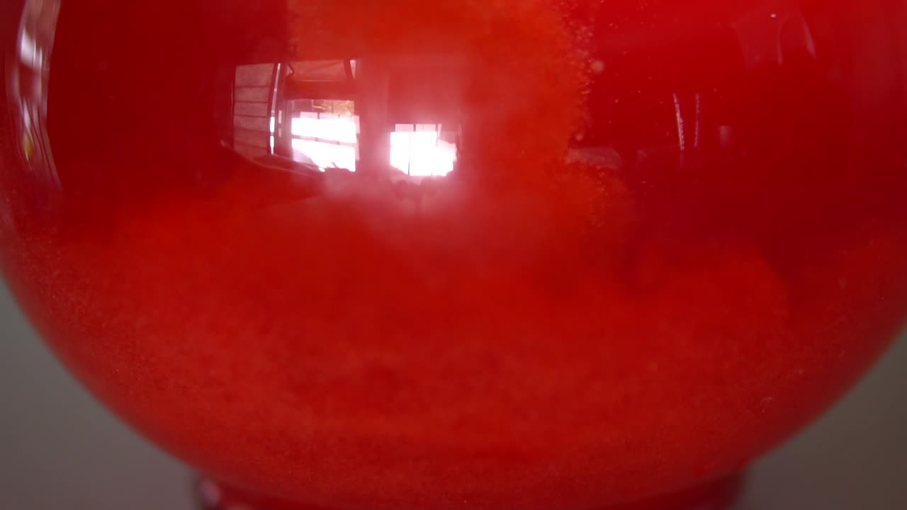 Red powder drink mix pouring into bottom of glass pitcher or water. Slow-mo