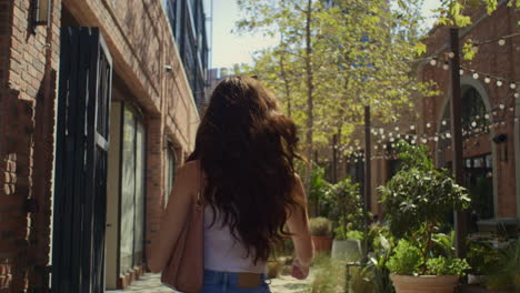 tranquil woman strolling on street back view. brunette walking near brick wall.