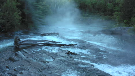 Aerial-drone-shot-flying-low-over-a-dark-misty-forest-river-and-the-Big-Wilson-Falls-waterfall-at-sunset-with-trees-in-silhouette