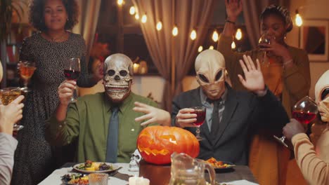 masked friends drinking and dancing at halloween dinner party