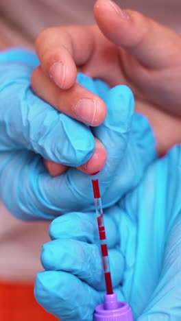 medical worker taking blood sample. hands in blue sterile gloves collecting blood from patient's finger. close-up. blood test. vertical video