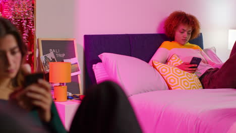 dos mujeres relajándose en una habitación por la noche usando teléfonos inteligentes