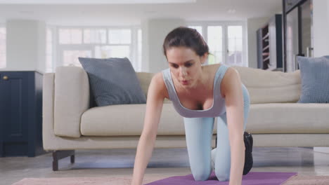 woman in fitness clothing at home in lounge doing stretches and exercising on mat - shot in slow motion