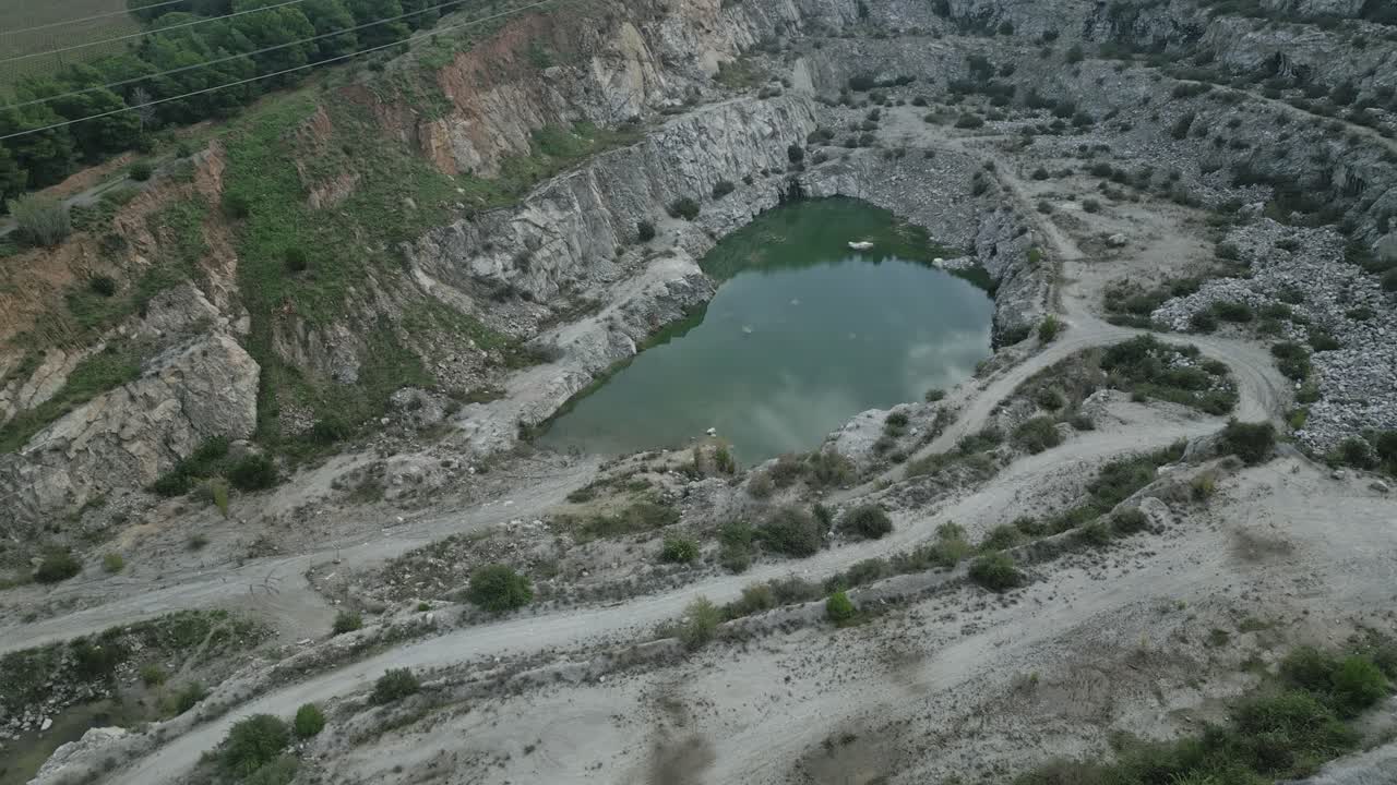 Green water filling abandoned quarry near sant fost de campsentelles, barcelona, reflecting sky and rugged terrain from high aerial perspective