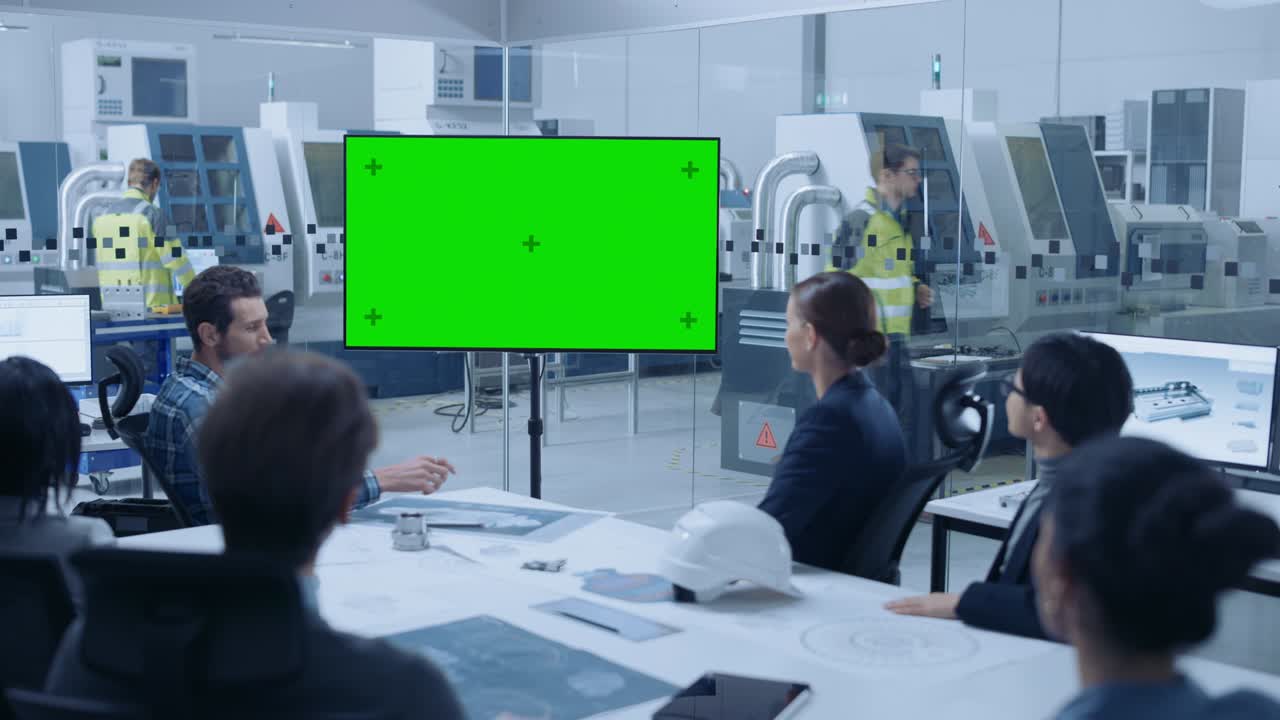 현대적인 공장 사무실: 회의 테이블에 앉아있는 엔지니어, 관리자 및 투자자의 다양한 팀, 그들은 녹색 화면을 보여주는 인터랙티브 tv에 손을 흔들고 있습니다.