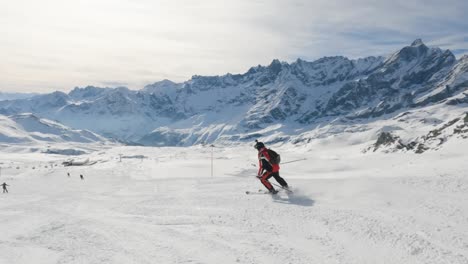 Follow-view-of-skier-descend-on-a-slope-in-Cervinia-ski-resort-with-rocky-mountain,-slow-motion