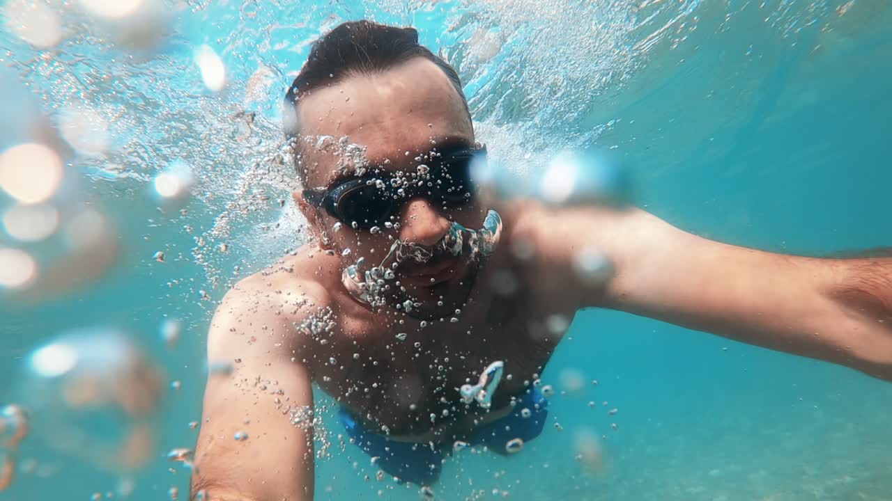 Un hombre con gafas de natación bajo el agua sosteniendo una cámara en el mar Egeo. Cámara lenta, grabación subacuática. Grecia.