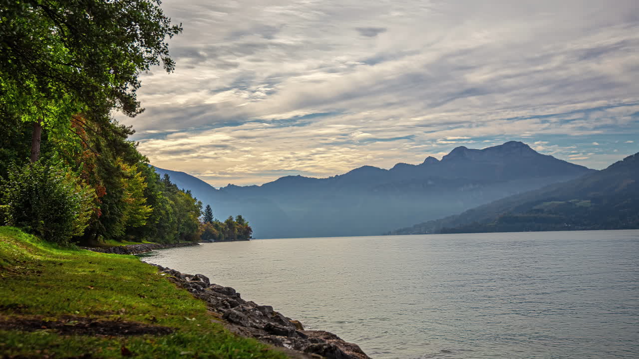 Timelapse from the shore of the beautiful attersee lake with a view of the calm waters reflecting the fast moving clouds and majestic alpine peaks in the background on a cold fall morning