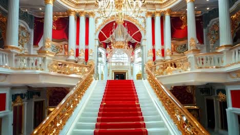 a red carpeted staircase in a grand building with a chandelier