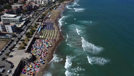 Fly-Over-of-People-on-a-Busy-Beach-with-Umbrellas-and-the-Sea-Promenade-Street