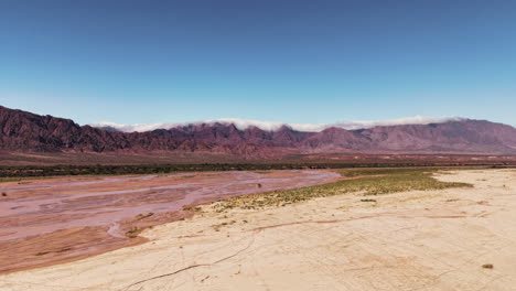 hyperlapse drone footage of a shallow river in the desert with the andes mountain range in the background, embraced by clouds