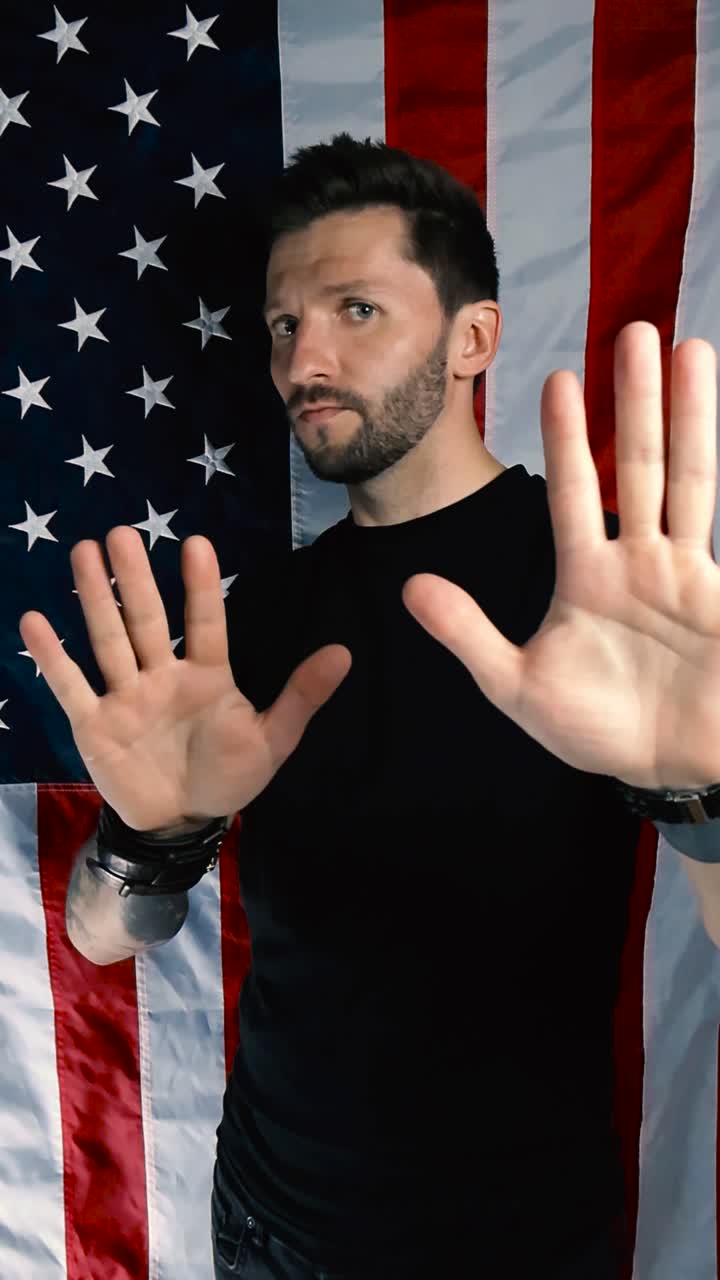Tattooed and handsome patriot male doing stop it motion or pushing away motion expression with his hands with a serious and not happy face in front of an American United states flag in slow motion
