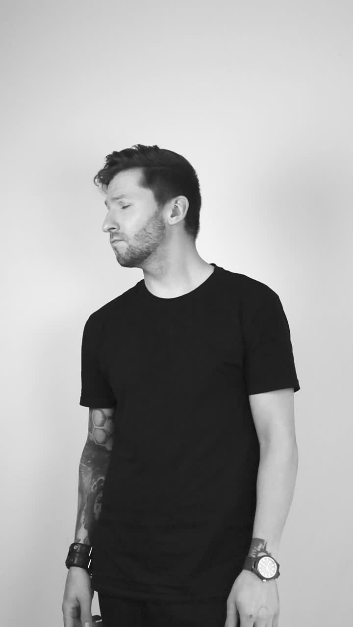 Grayscale video of a white man with tattoos and short beard raising his finger and waving it showing that he does not like something and that the viewer should stop what they are doing.