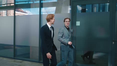 two men top managers workers discussing business plans walking outdoors along office building. businessmen in formal suits communicating to each other while going to work