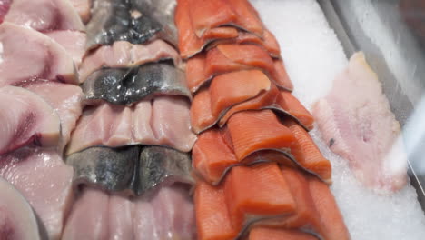 various types of fish in seafood market display case, fresh raw fish fillets neatly stacked on ice in fishmongers shop case, dolly out hd