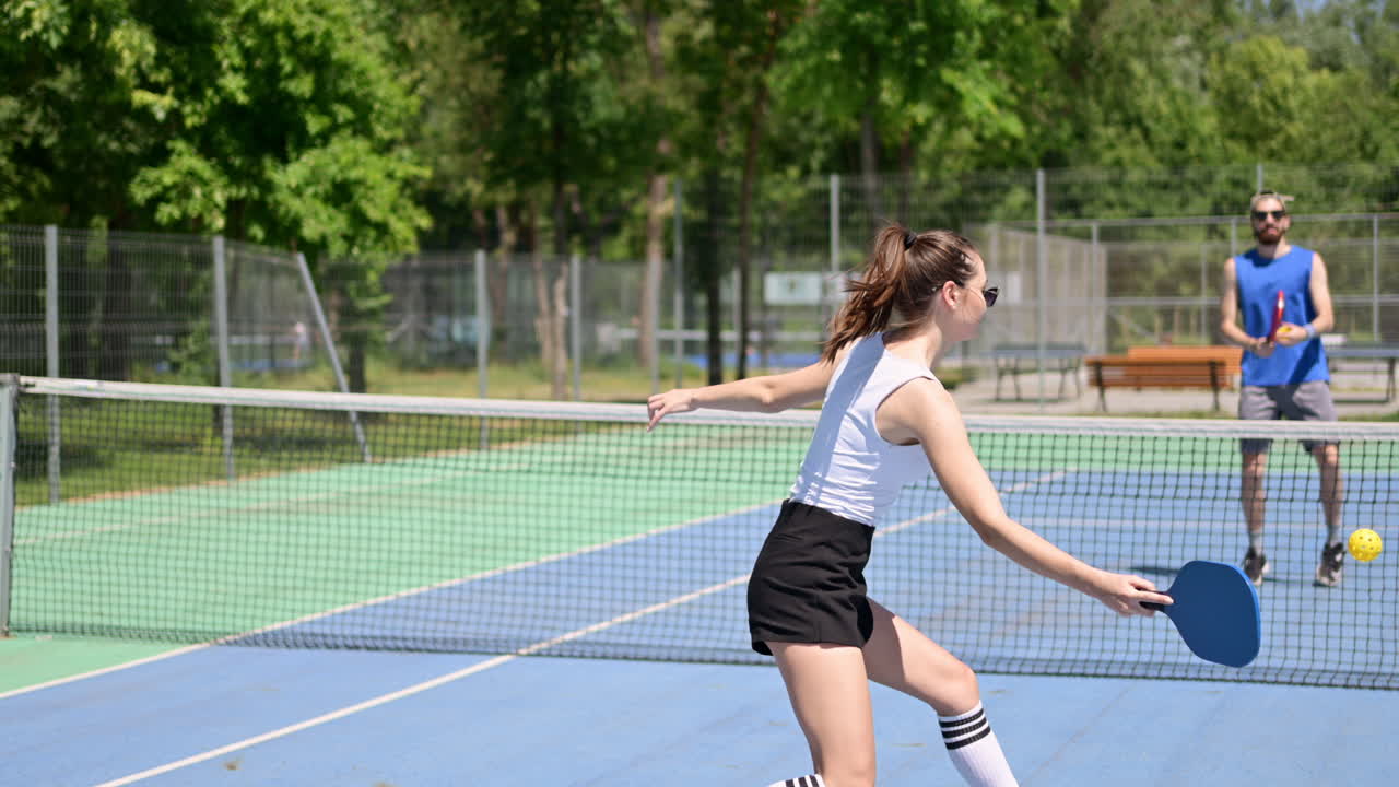 Woman playing pickleball on a blue and green court on a sunny day