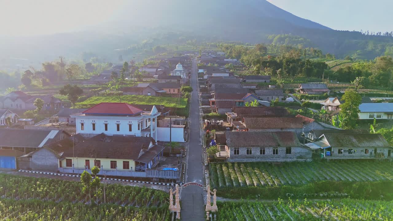 Beautiful view of Indonesia Village with mountain on the background in sunny morning. Aerial view of Stabelan Village on slope of Mount Merapi Volcano, Indonesia. Drone flying backward.