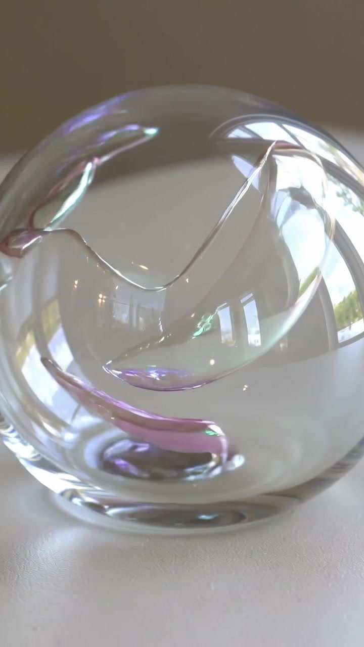 Vertical video: Daylight shifting causing colored ribbon uncoiling in glass orb on table by window