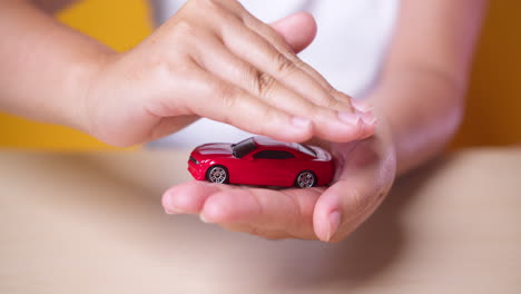 Hand-woman-protect-with-her-hands-a-red-car,-concept-for-insurance,-buying,-renting,-fuel-or-service-and-repair-costs