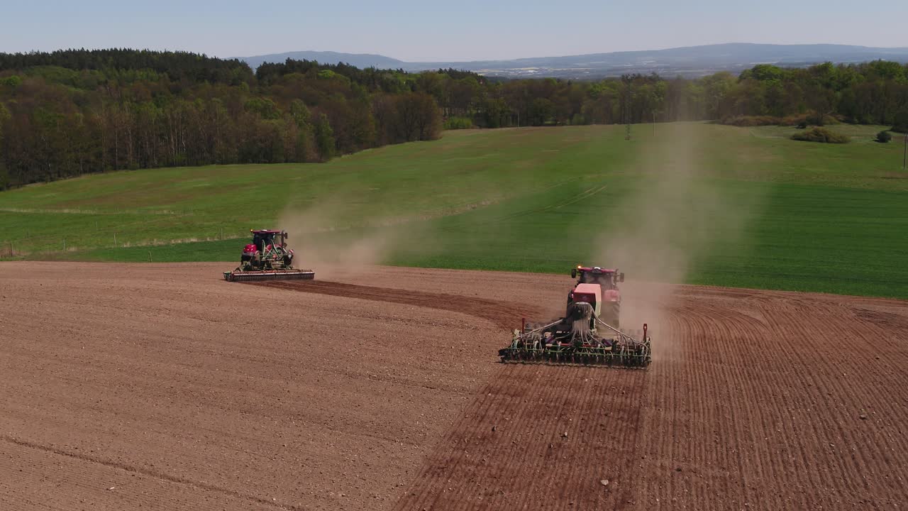 Two red tractors work on dry soil fields near Prague with clear weather and intense sunlight