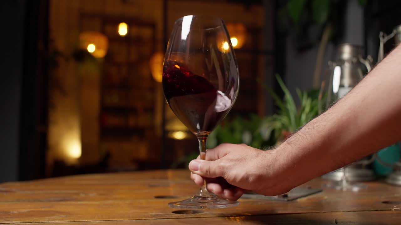 Right hand gently swings red wine inside a glass, set against a cozy, relaxing home backdrop